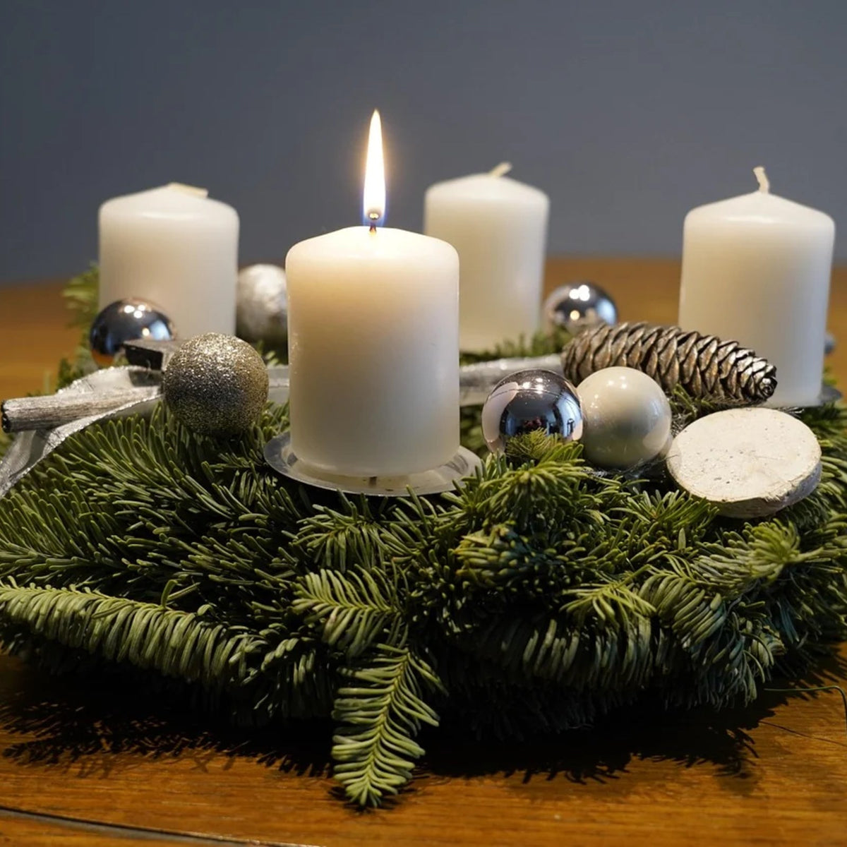 Fertiger Adventskranz aus Tannengrün mit vier weißen Kerzen und Zapfen auf einem Holztisch